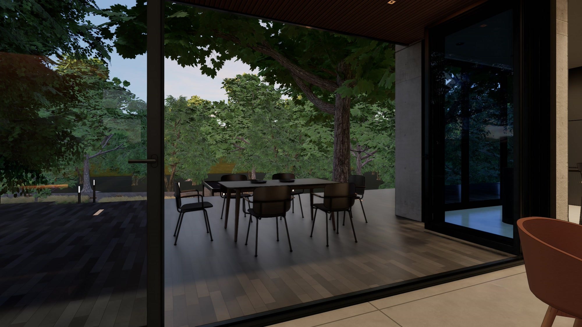 View from the living room through black-framed glass doors to a shaded timber deck with a dining table among mature trees